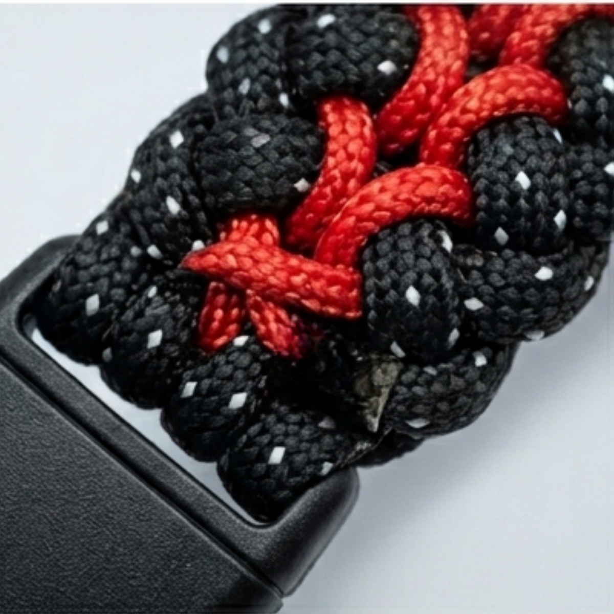 Close-up of a black and red paracord watch strap with a black plastic buckle, shown against a light gray background.