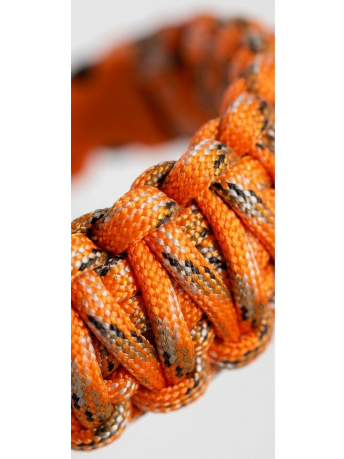 Close-up of an orange paracord bracelet with black and gray patterned details, shown against a light gray background.